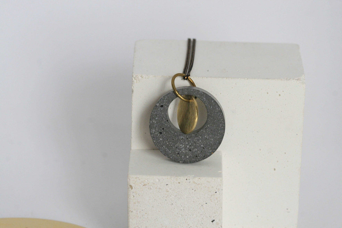 Beton ketting met gouden accent, op witte blok, minimalistisch en uniek