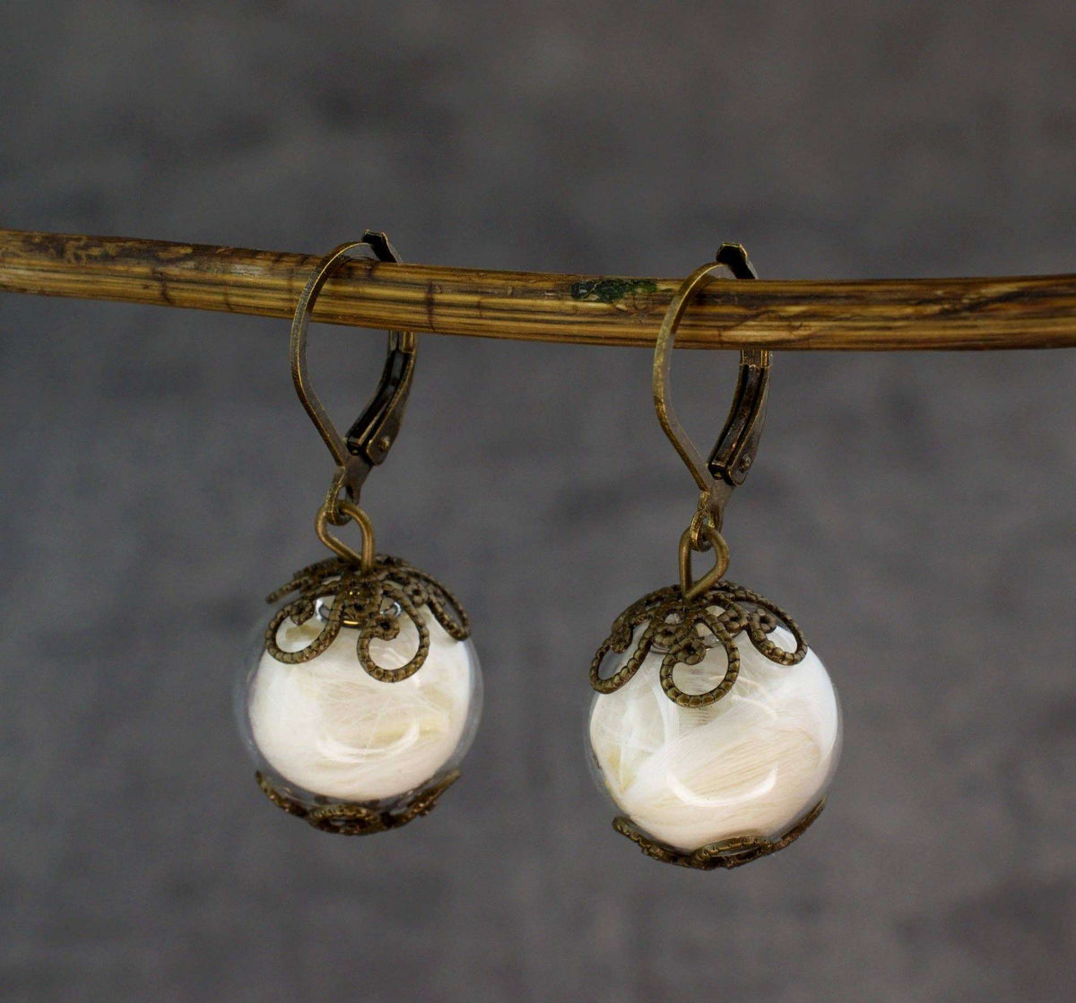 Close-up van gouden oorbellen met glazen bol en decoratieve metalen details, handgemaakt, RAAK oorringen veer