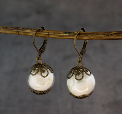 Close-up van gouden oorbellen met glazen bol en decoratieve metalen details, handgemaakt, RAAK oorringen veer